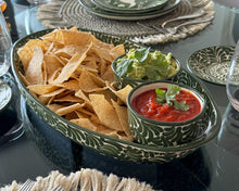 Load image into Gallery viewer, A green and beige patterned ceramic serving tray filled with tortilla chips and two small bowls of guacamole and salsa, set on a dining table with woven placemats and matching plates.
